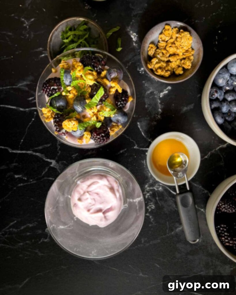 One completed berry yogurt parfait and the second one with the first layer of yogurt in a stemless martini glass.