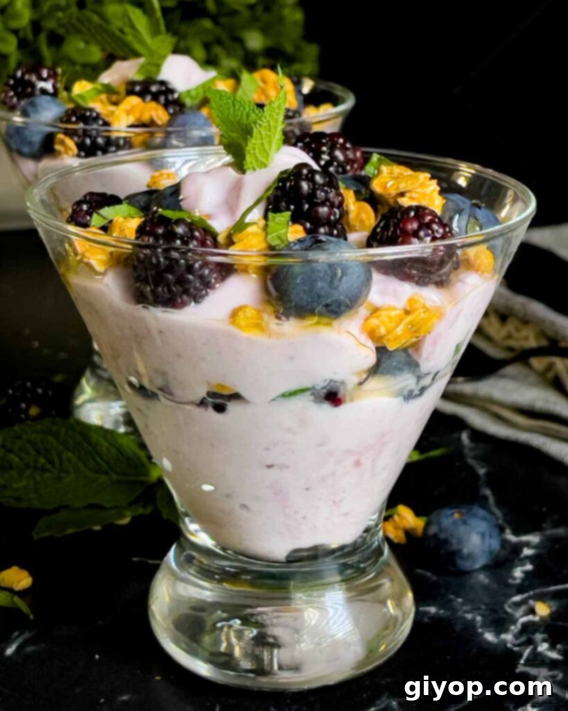 Berry yogurt parfait in a stemless martini glass on a dark surface.