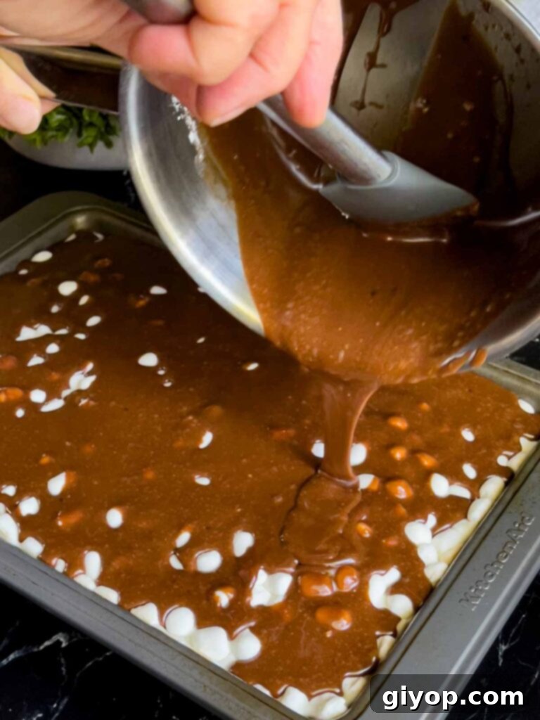 Warm chocolate frosting being generously poured over the melted mini marshmallows on top of the Mississippi Mud Cake, creating a smooth, glossy layer.