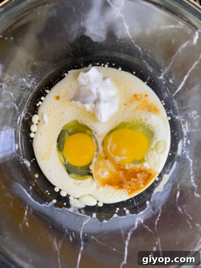 Wet ingredients for Mississippi Mud Cake, including eggs, oil, milk, sour cream, and vanilla, in a clear glass mixing bowl.