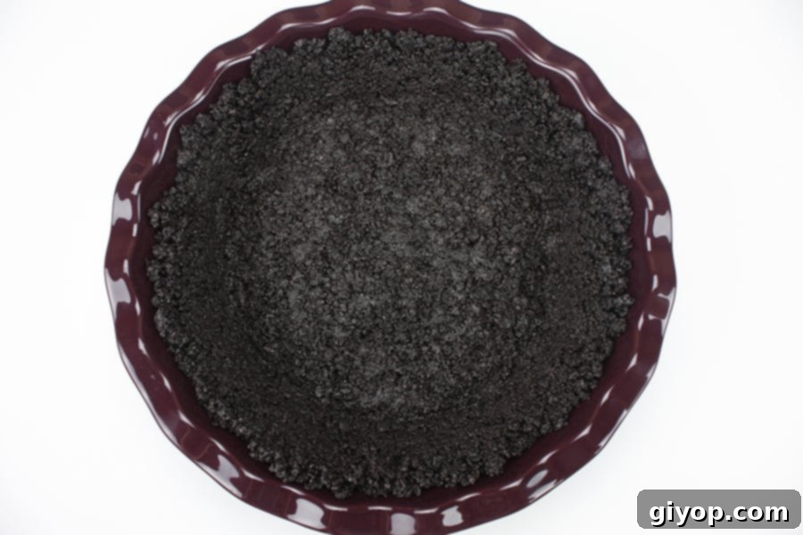 Crushed Oreo cookies evenly pressed into the bottom and sides of a vibrant purple pie plate, forming a firm base ready for the pie filling.