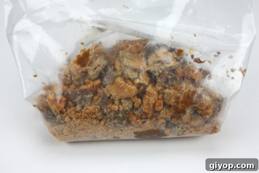 A clear, resealable zip-top bag filled with perfectly crushed Butterfinger candy bars, their distinctive texture visible, ready to be incorporated into the pie filling.