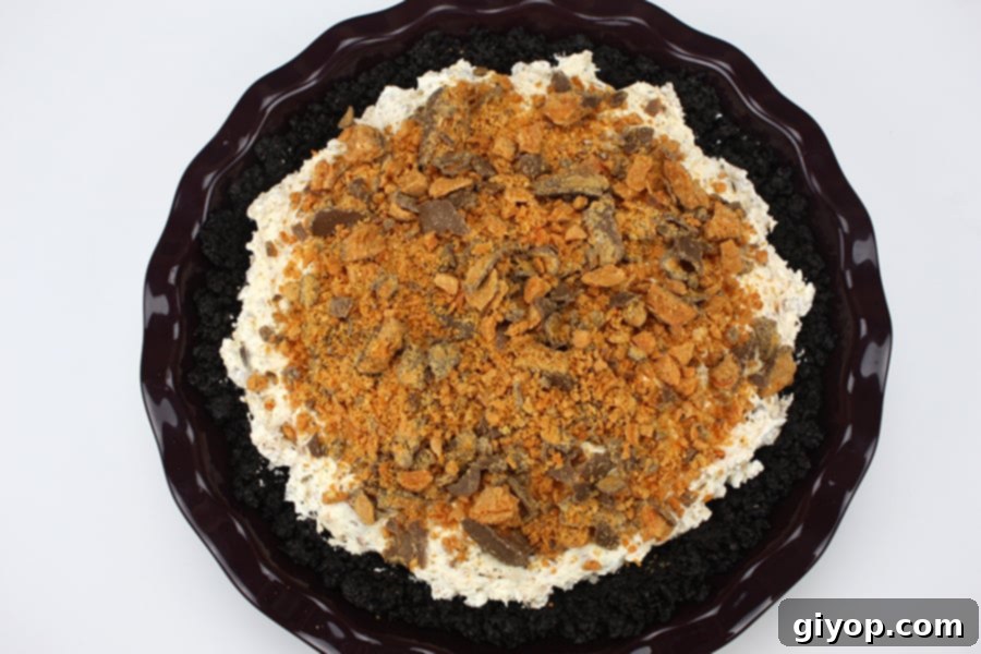 The fully assembled Butterfinger pie, with its creamy, speckled filling spread smoothly over the chocolate cookie crust in a purple pie plate, glistening and ready for its essential chilling period.