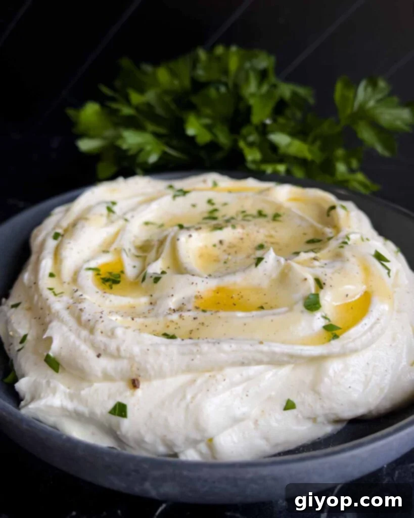Whipped feta garnished with honey, chopped parsley, and black pepper in a dark bowl.