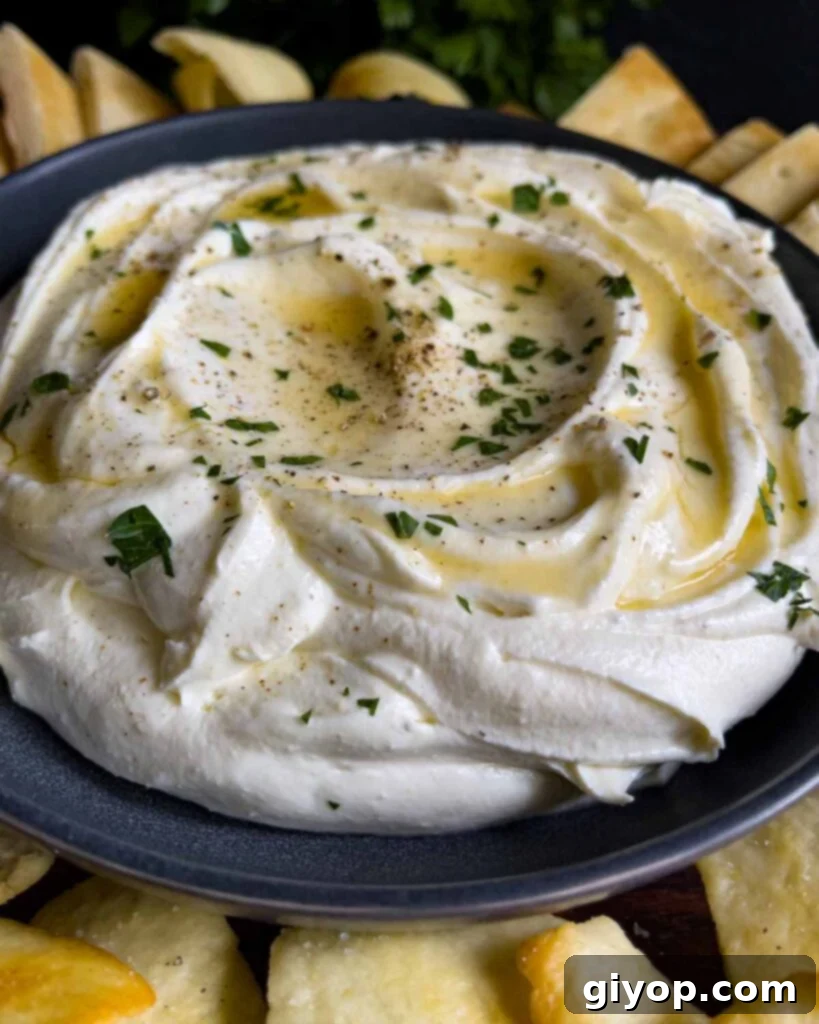 Whipped feta garnished with honey, chopped parsley, and black pepper in a dark bowl surrounded by pita chips and pita bread.