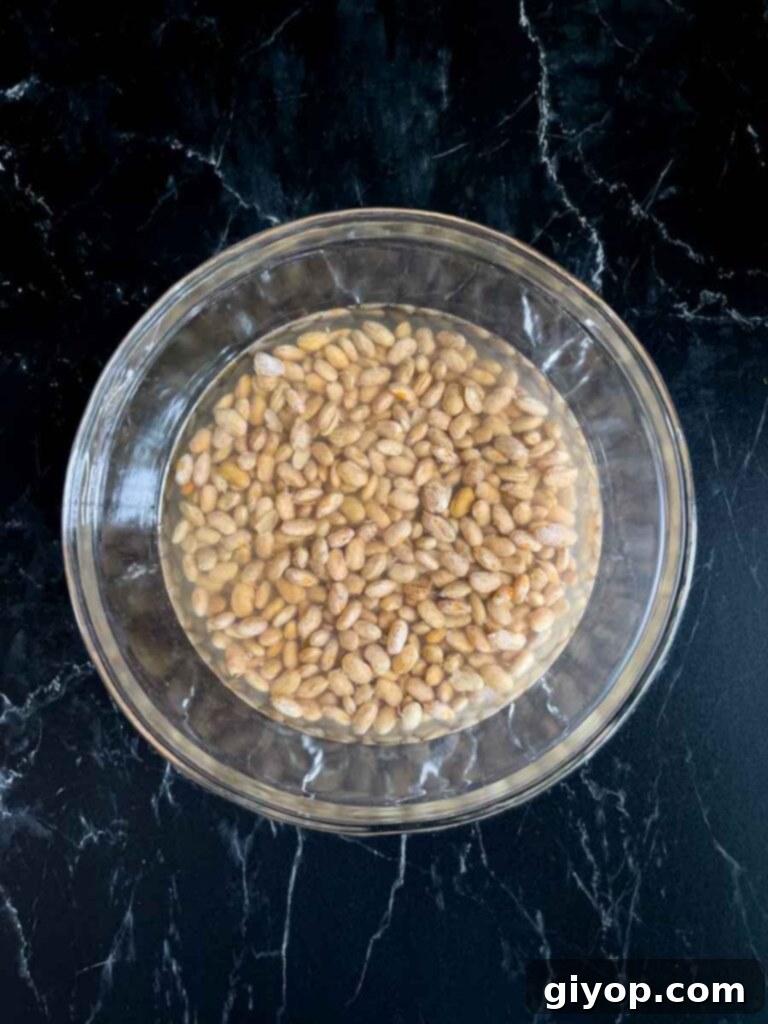 Pinto beans soaking in water in a glass bowl.