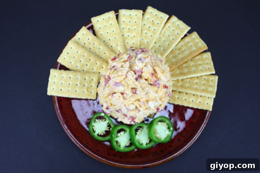 The Secret to Irresistible Homemade Pimento Cheese 3 A close-up of Pimento Cheese in the center of a red plate surrounded by a generous scattering of crackers and vibrant sliced jalapeños.