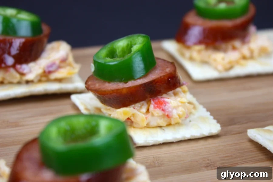 The Secret to Irresistible Homemade Pimento Cheese 5 Pimento Cheese spread generously on crackers, topped with slices of smoked sausage and fresh jalapeno, ready to be enjoyed.