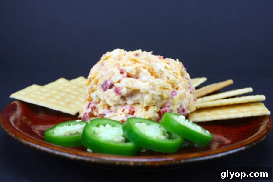 The Secret to Irresistible Homemade Pimento Cheese 6 A vibrant red plate showcasing a generous serving of homemade Pimento Cheese, surrounded by a medley of crispy crackers and fresh, thinly sliced jalapeños.