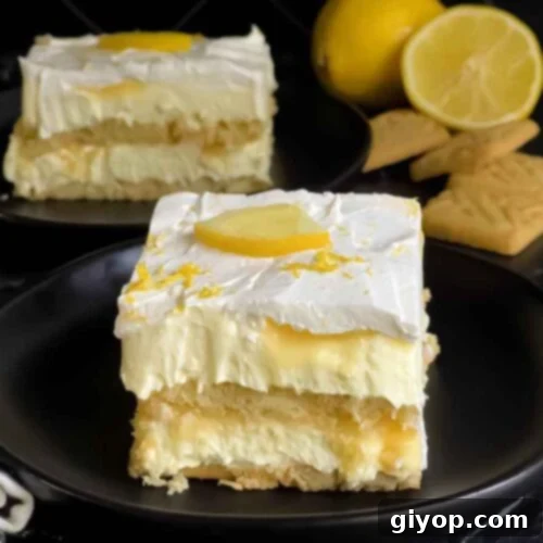 A serving of Lemon Icebox cake garnished with a lemon slice and zest on a dark plate.