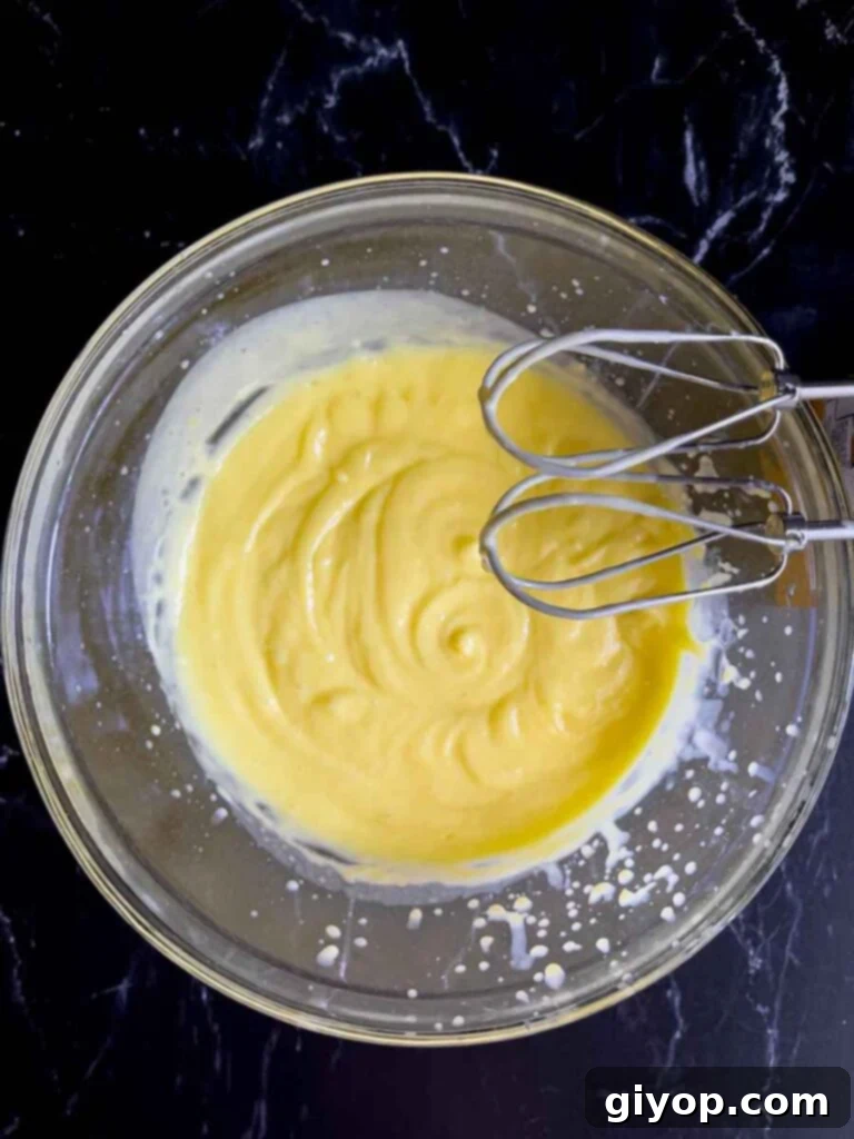 Creamy lemon pudding and milk mixture being prepared in a clear glass mixing bowl, essential for the lemon icebox cake.