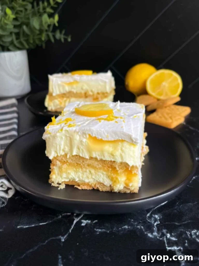A perfectly portioned serving of Lemon Icebox Cake, garnished with a fresh lemon slice and vibrant zest, presented on a dark plate.