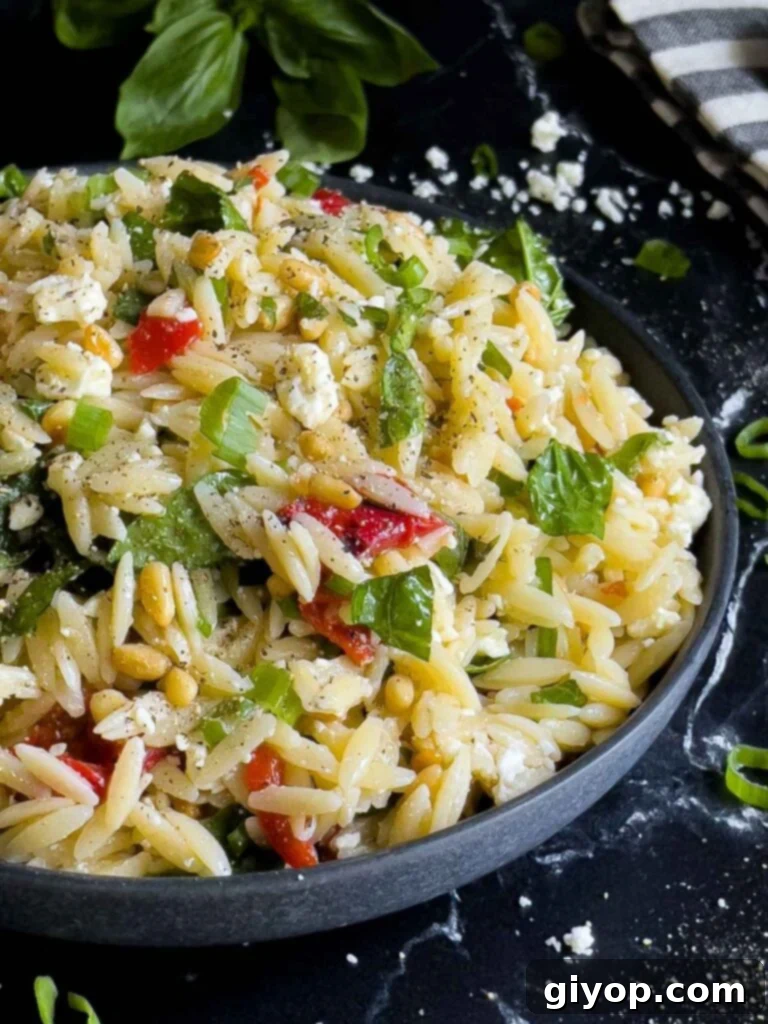 A dark bowl filled with vibrant Spinach and Feta Orzo Salad, garnished with fresh herbs, resting on a dark surface.