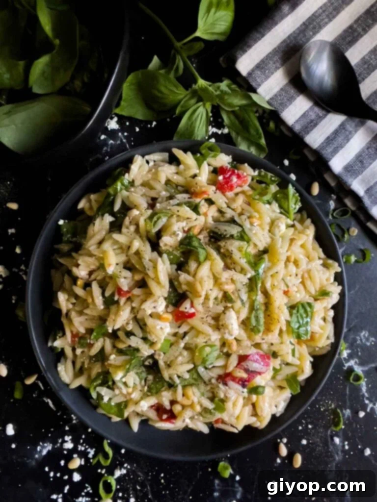 A dark bowl brimming with a beautifully presented Spinach and Feta Orzo Salad, ready to be served, on a dark countertop.