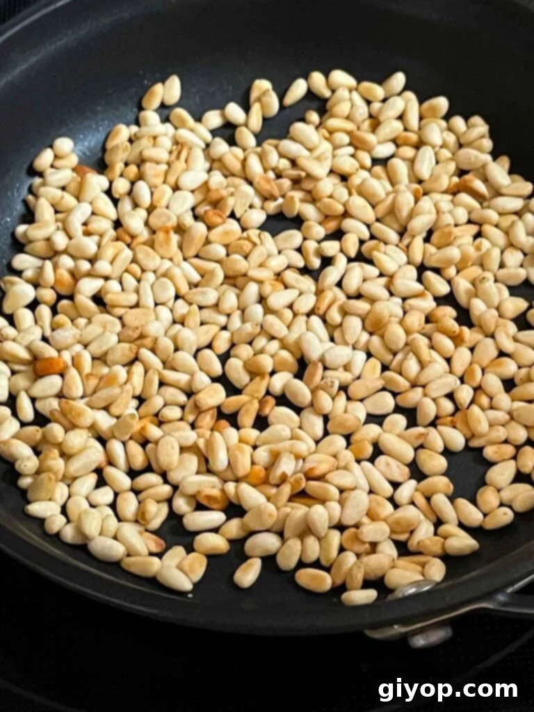 Pine nuts being toasted to a golden perfection in a dry skillet over medium-low heat, emitting a fragrant aroma.