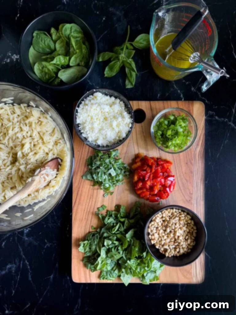 Freshly chopped spinach, basil, roasted red peppers, and green onions, ready to be incorporated into the orzo salad, displayed on a dark surface.