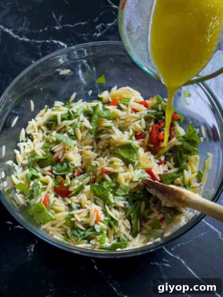 The zesty dressing being drizzled over the colorful spinach and feta orzo salad, ready to be tossed for even coating.