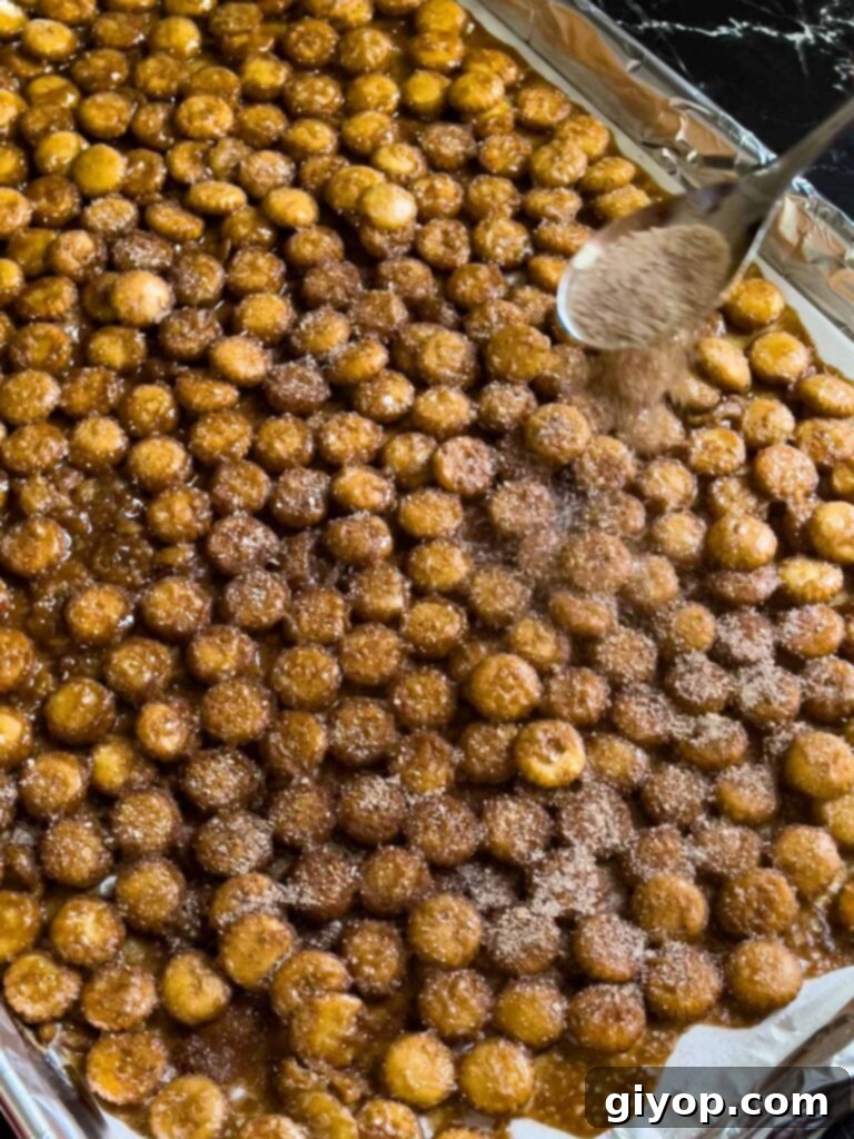 Adding cinnamon sugar to the hot oyster cracker churro snack mix after baking.