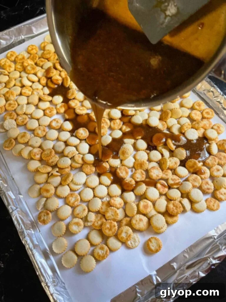 Pouring the toffee mixture over the oyster crackers on a lined baking sheet.