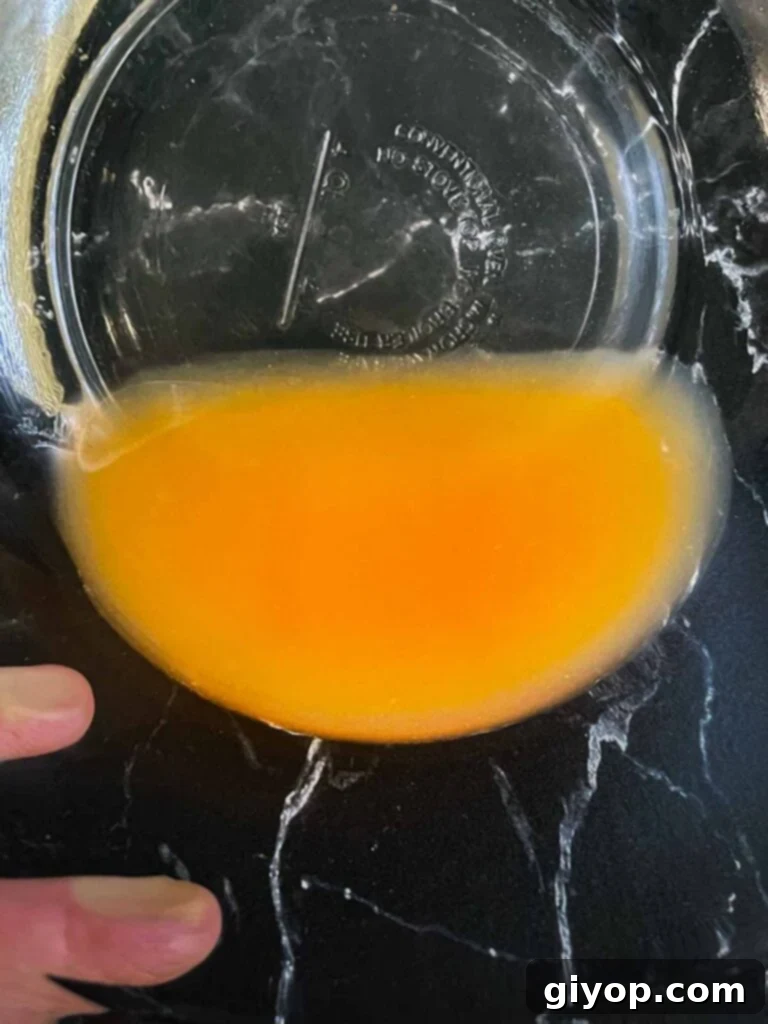 A glass bowl collecting the clear, golden peach juices that have drained from fresh peaches, preparing them for a perfect pie filling.