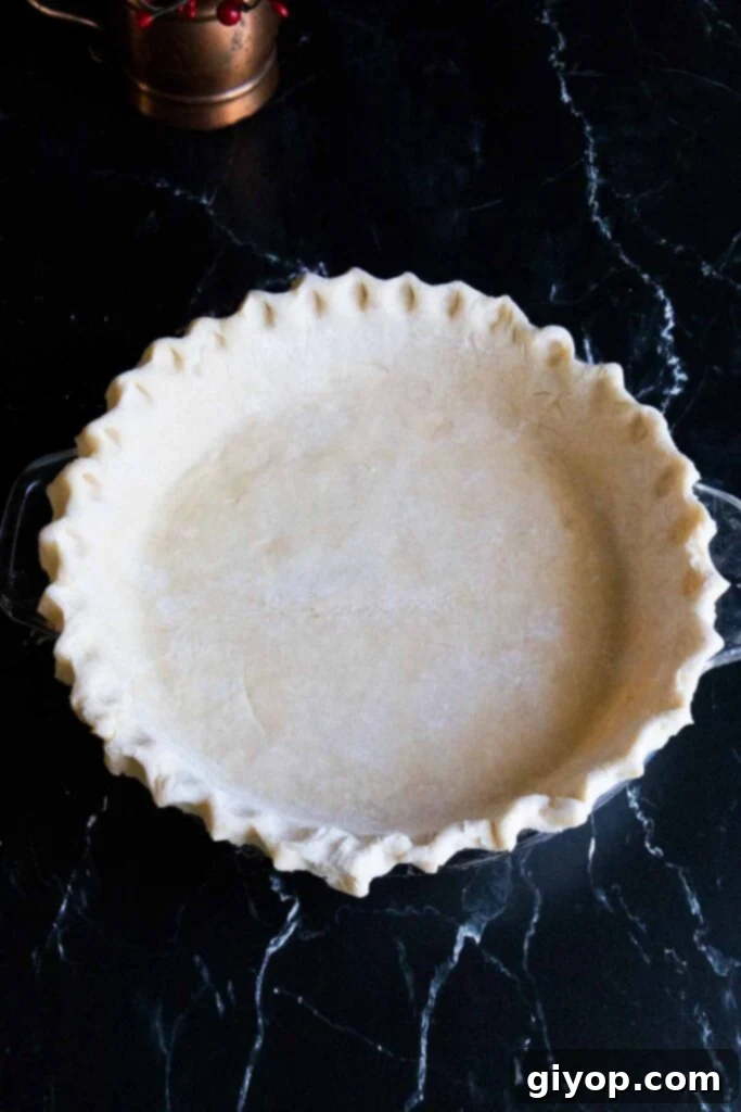 Perfectly Flaky Pie Crust 2 Fluted pie dough on a dark surface, showcasing beautiful crimped edges.