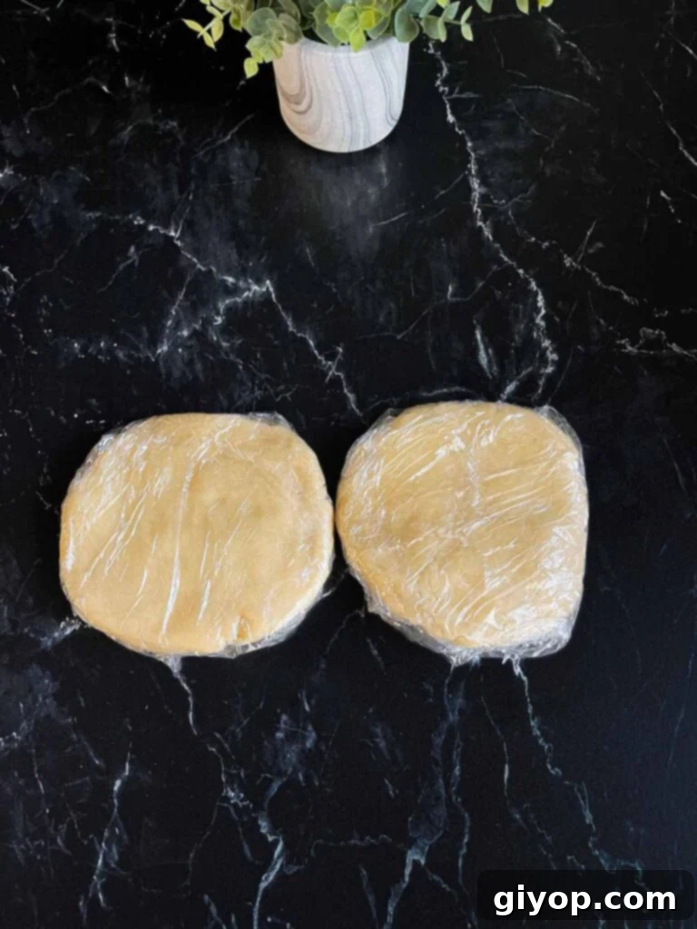 Perfectly Flaky Pie Crust 9 Pie crust dough disks wrapped in plastic wrap on a dark surface.