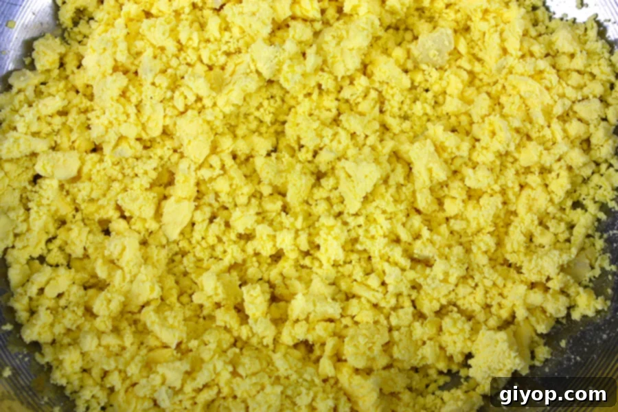 Smashed egg yolks in a metal mixing bowl, ready to be combined with other ingredients.