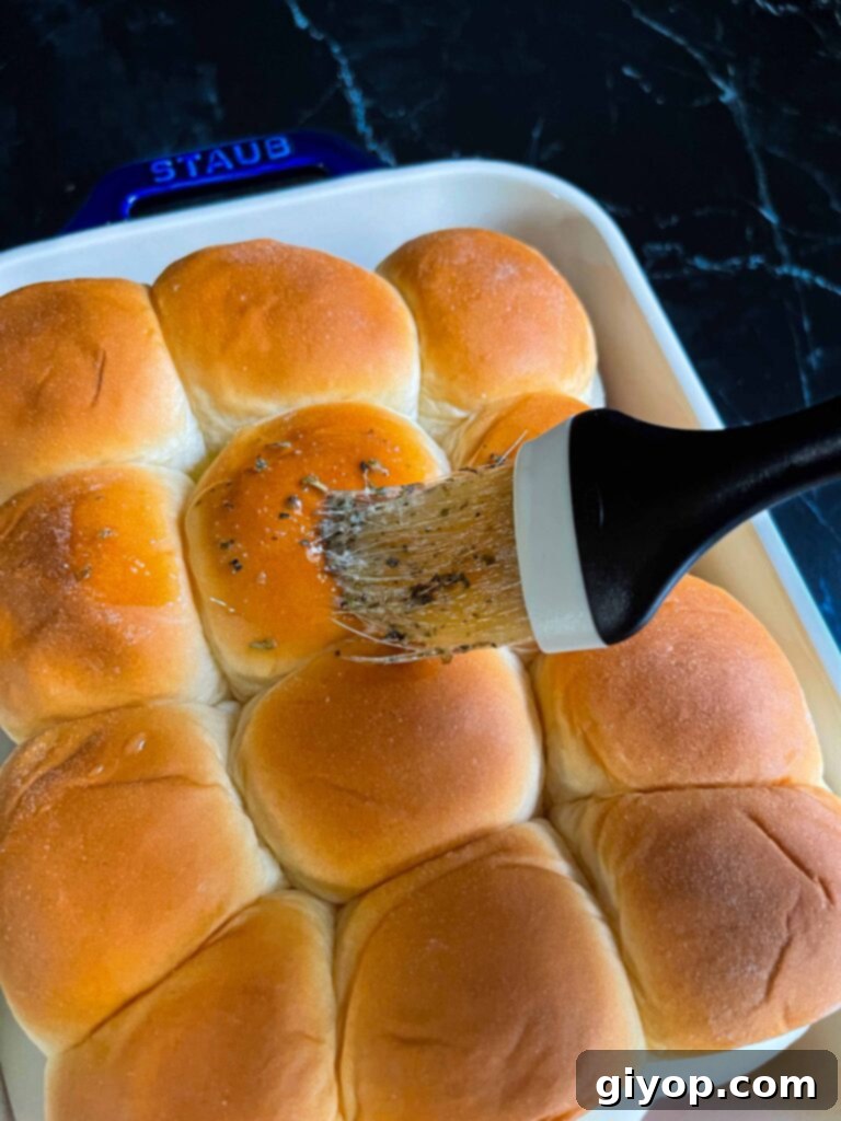 Cheesy Baked Chicken Parmesan Sliders 13 A culinary brush applying the aromatic butter-herb mixture to the tops of the chicken parmesan slider rolls.