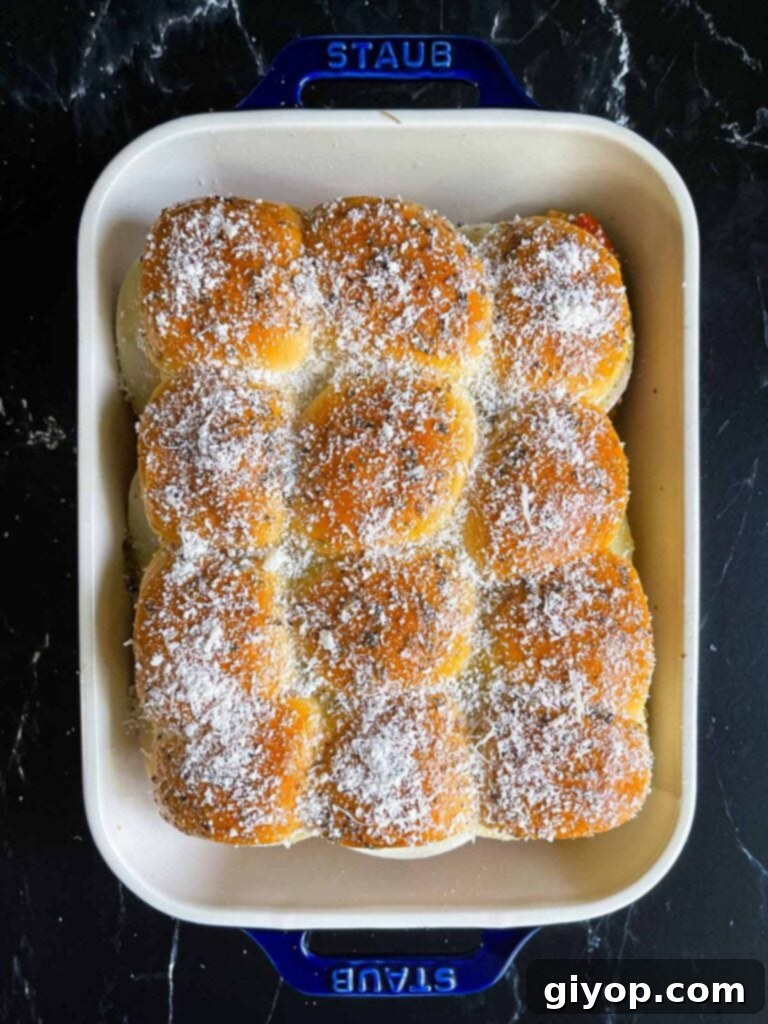 Cheesy Baked Chicken Parmesan Sliders 15 Chicken parmesan sliders generously topped with grated parmesan cheese in a baking dish, ready for the oven.