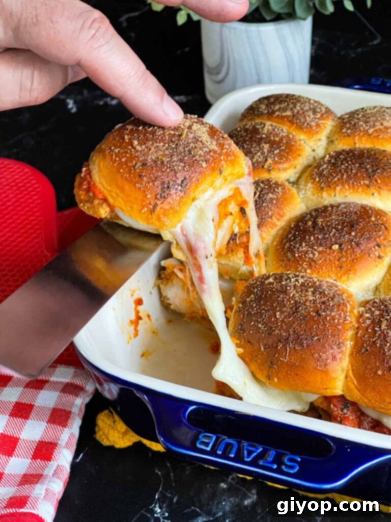 Cheesy Baked Chicken Parmesan Sliders 17 A single, perfectly baked chicken parmesan slider being lifted from the baking dish, showcasing its cheesy interior.