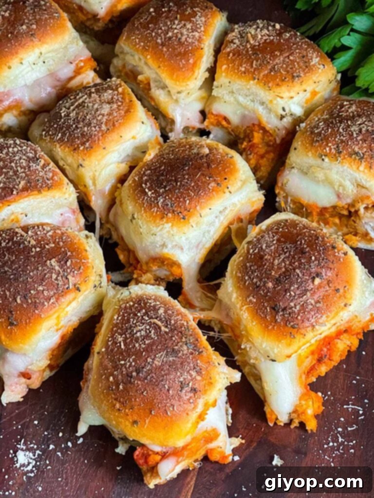 Cheesy Baked Chicken Parmesan Sliders 3 A close-up of chicken parmesan sliders garnished with fresh parsley on a wooden cutting board.