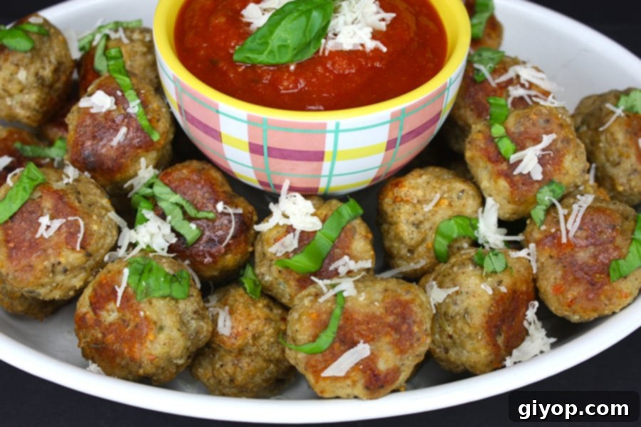 Close-up of a plate of baked chicken parmesan meatballs with fresh basil and cheese.