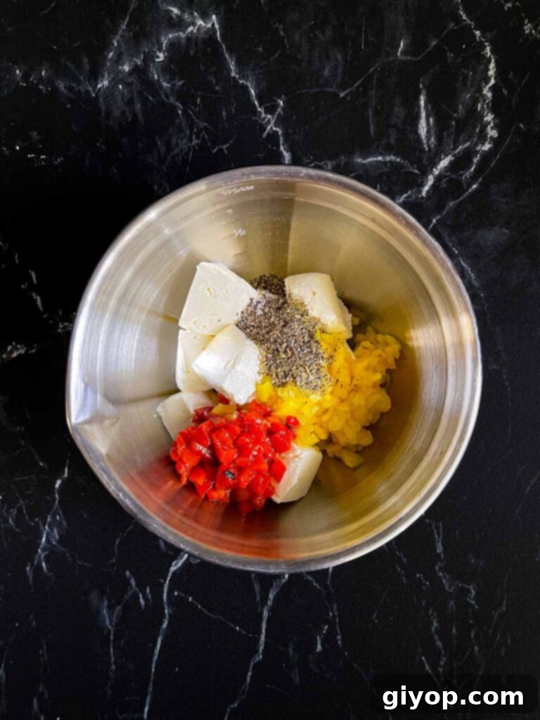 Ingredients for a cream cheese mixture for italian pinwheels in a silver mixing bowl on a dark surface.