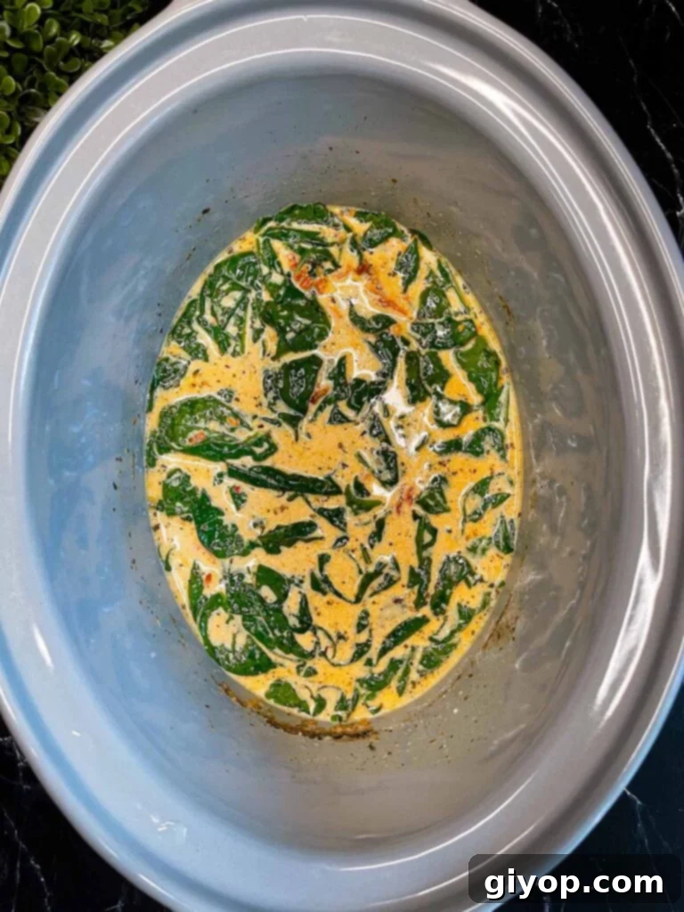 The rich and creamy Slow Cooker Tuscan Chicken sauce, infused with wilted spinach, bubbling gently in the crock pot.