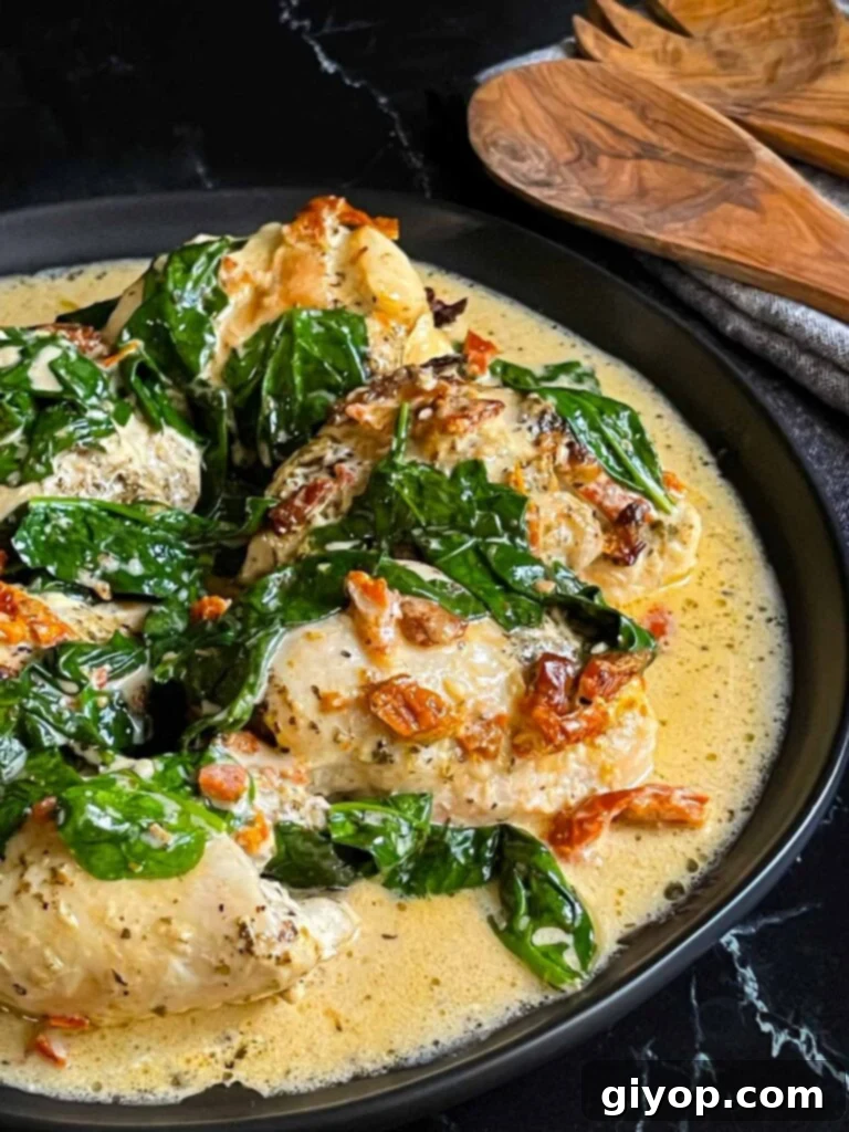 A close-up shot of the finished Slow Cooker Tuscan Chicken, featuring tender chicken pieces in a creamy, vibrant sauce, served in a dark bowl on a dark surface.