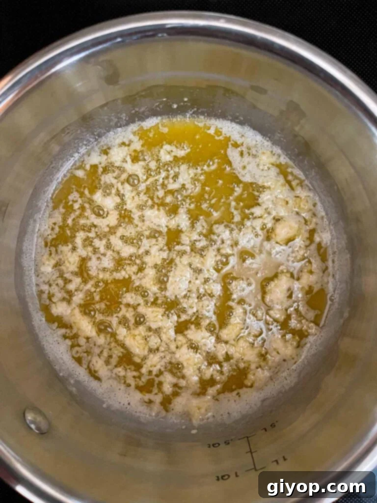 Melted butter and sun-dried tomato oil shimmering in a small saucepan, with freshly minced garlic just added and beginning to sauté.