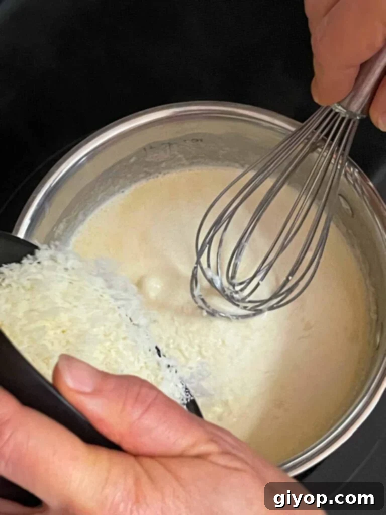 Grated Parmesan cheese being gradually whisked into the warm, creamy sauce in a saucepan.