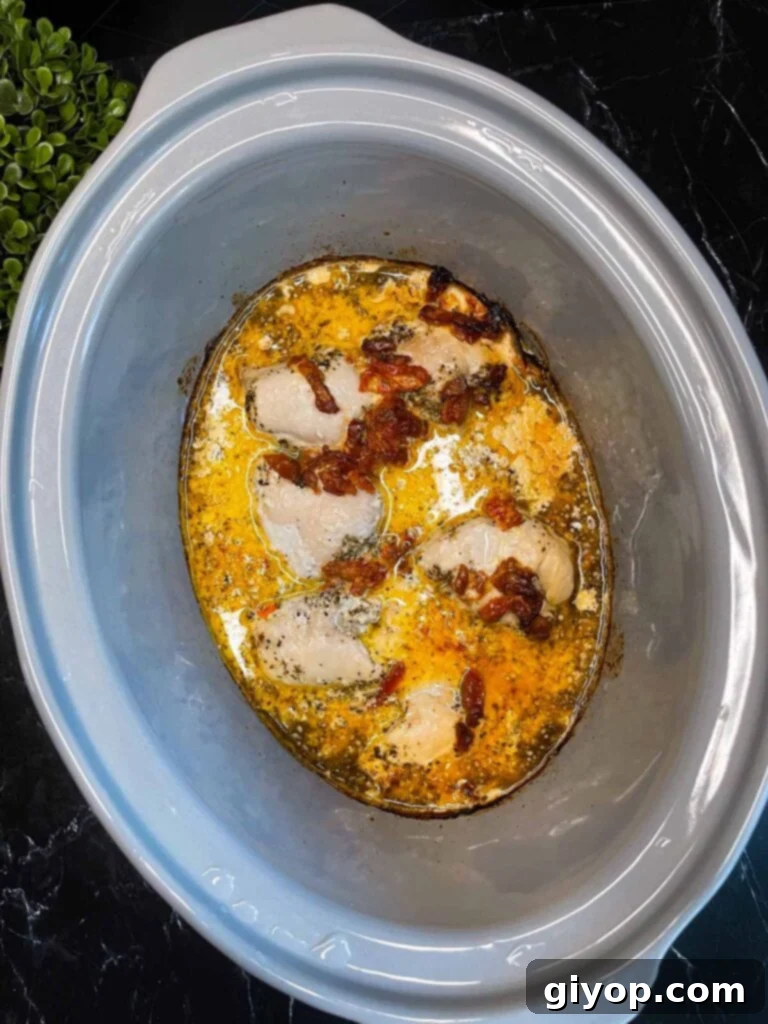 Fully cooked Slow Cooker Tuscan Chicken simmering in its creamy sauce within the slow cooker, ready for the final touches.