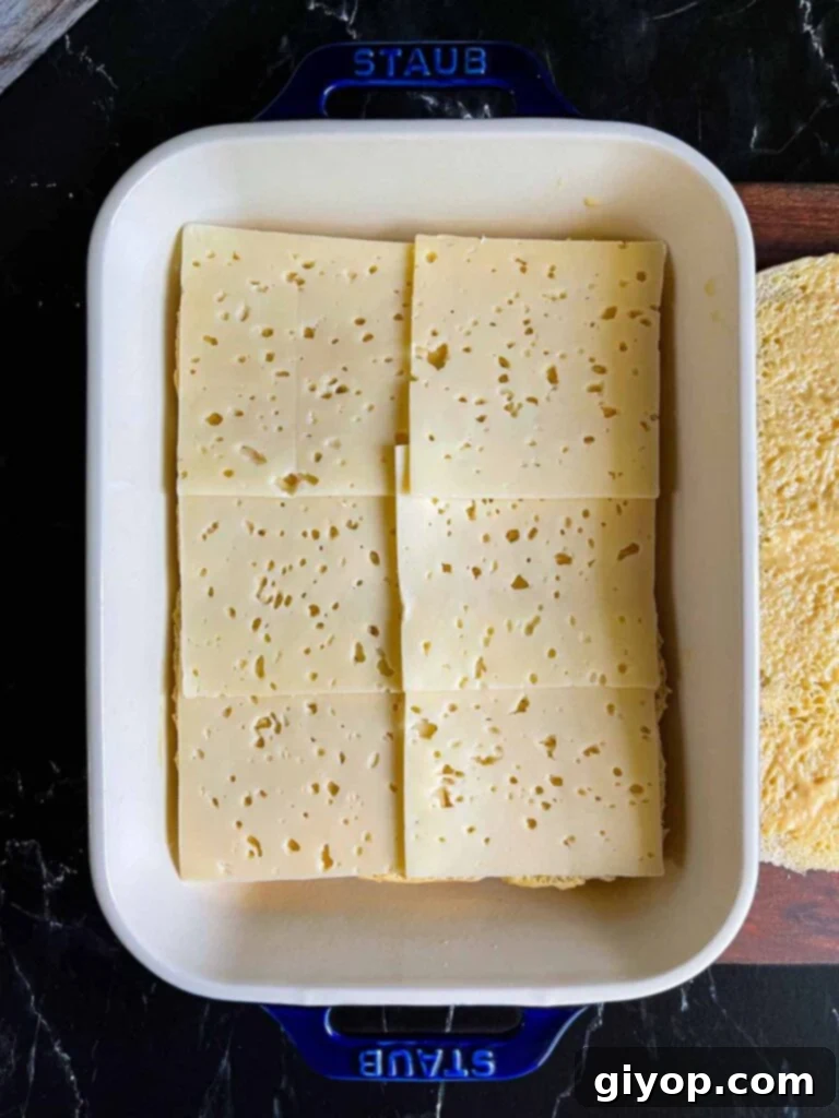 Swiss cheese layered over slider rolls in a baking dish.