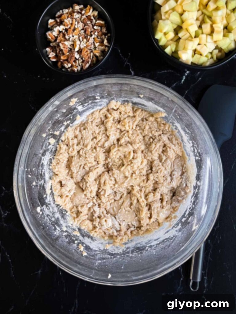 Dry ingredients mixed into the wet ingredients for apple dapple cake in a glass bowl on dark surface.