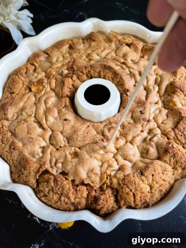 Holes being poked into the baked apple dapple cake in a bundt pan on a dark surface.