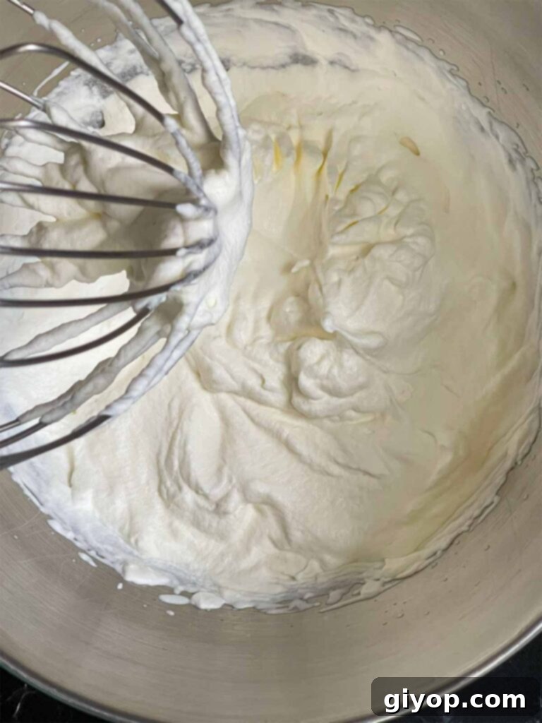 Heavy cream, perfectly whipped to stiff peaks, standing tall in a shiny metal mixing bowl, ready for frosting preparation.