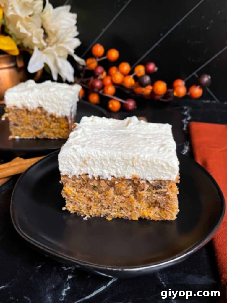 A perfectly frosted slice of sweet potato cake, topped with fluffy white cream cheese frosting, presented on a dark plate on a dark surface.