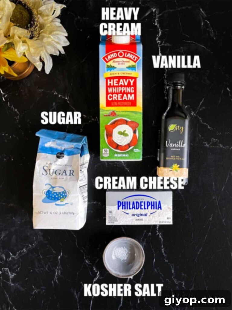 Ingredients for whipped cream cheese frosting, including blocks of cream cheese, heavy cream, and vanilla extract, laid out on a dark surface.