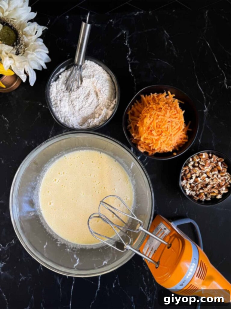 Wet ingredients for sweet potato cake, a creamy blend of eggs, sugar, oil, and vanilla, combined in a large glass bowl on a dark surface, ready for dry ingredients.