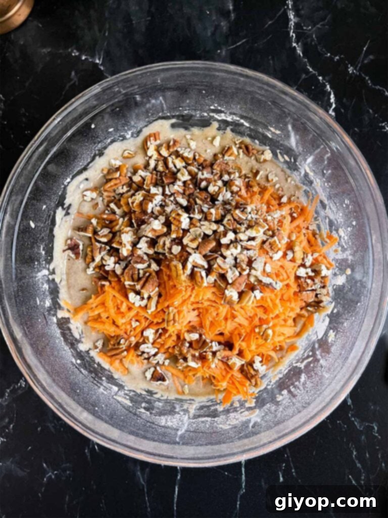Finely shredded fresh sweet potato and toasted chopped pecans added to the cake batter in a clear glass mixing bowl, ready to be folded in.