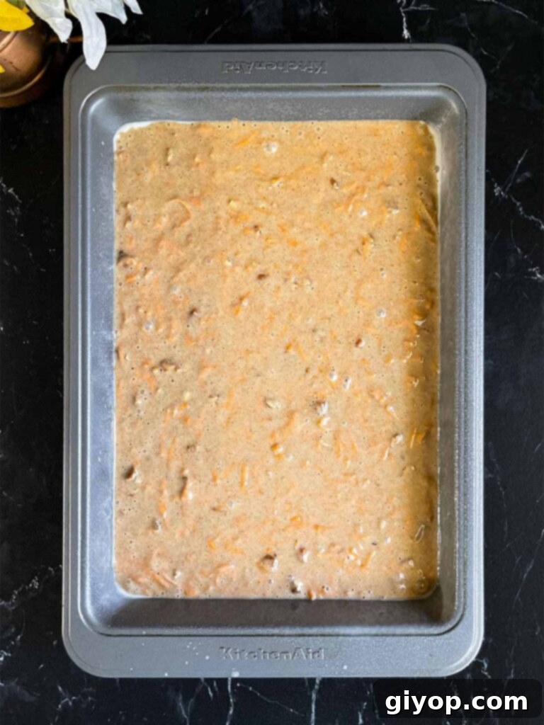 Smooth sweet potato cake batter poured evenly into a 9x13 inch baking pan, ready for the oven, on a dark surface.