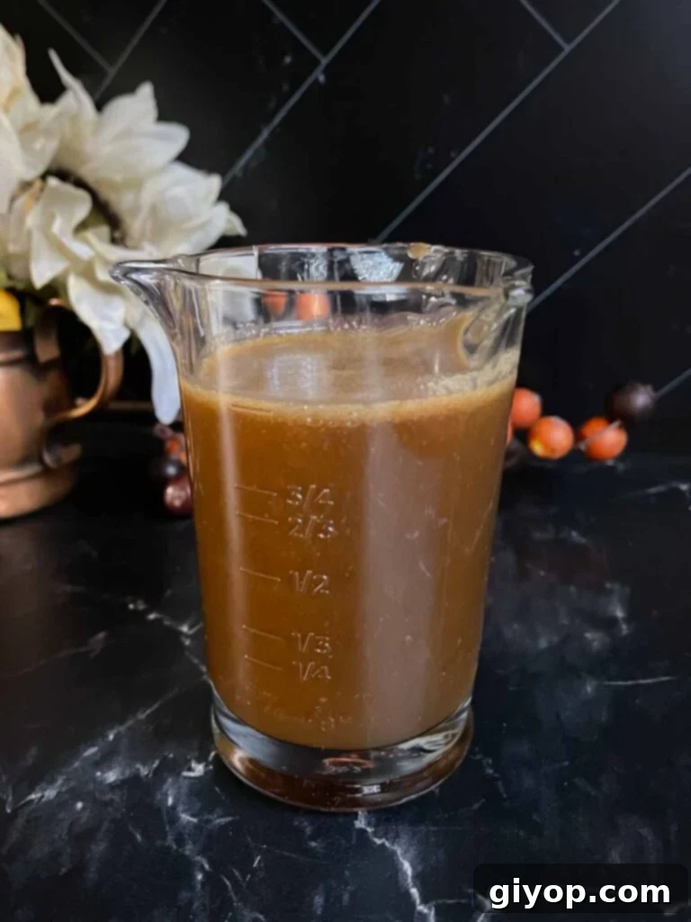 Decadent Pumpkin Bread Pudding with Salted Caramel Drizzle 11 Salted caramel sauce in a glass measuring cup on a dark surface.
