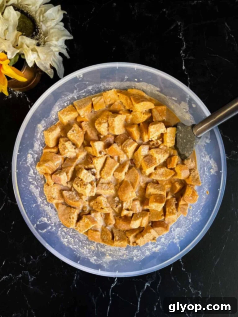Decadent Pumpkin Bread Pudding with Salted Caramel Drizzle 7 Bread mixed with the custard ingredients for pumpkin bread pudding in a large bowl on a dark surface.