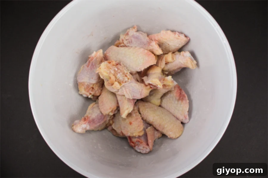 Raw chicken wings coated in baking powder and salt in a white bowl, ready for baking.